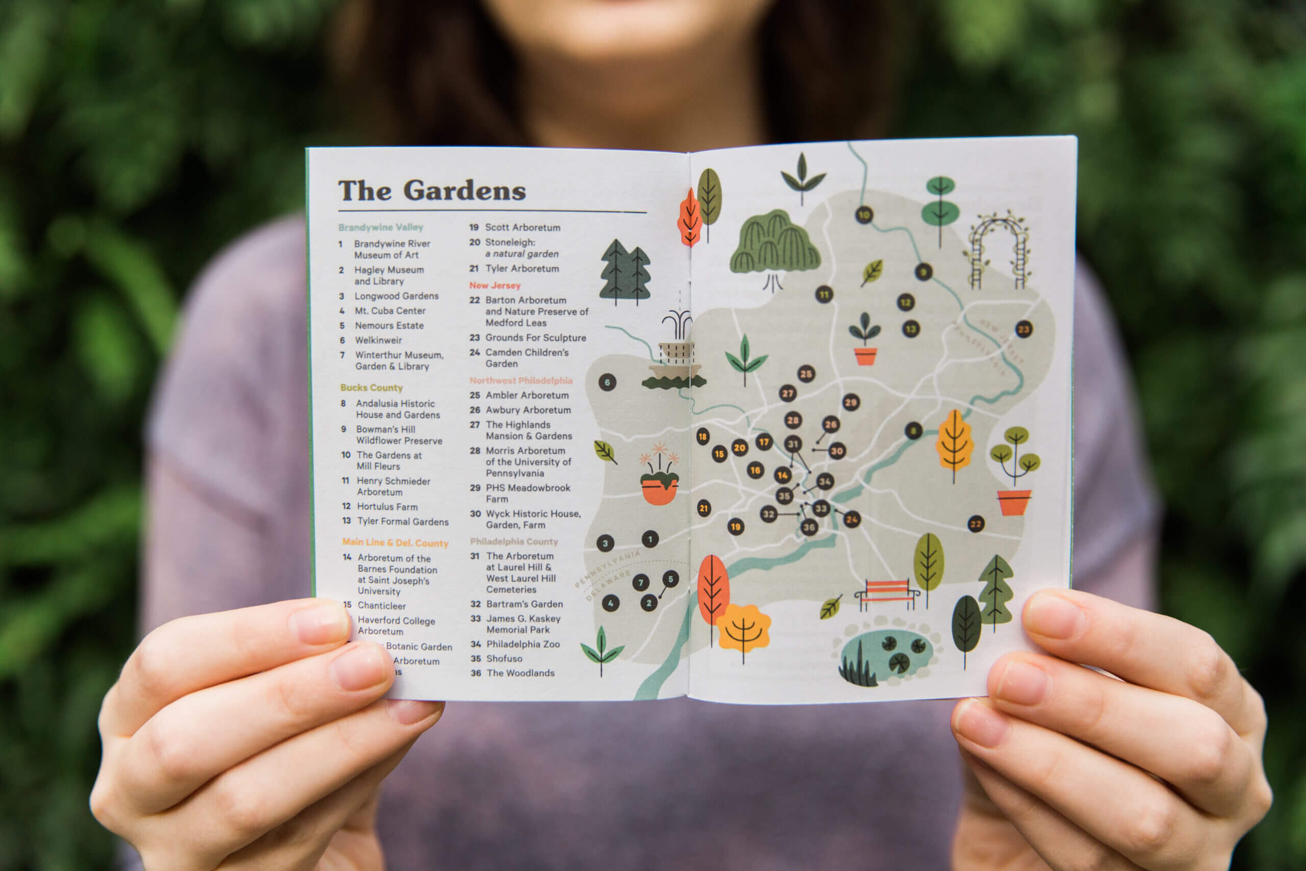 Hands opening a pamphlet to a page that shows various gardens in the area