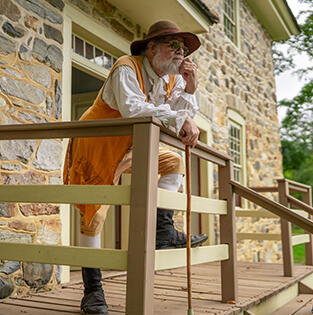 Historical reenactor in colonial attire standing on a porch