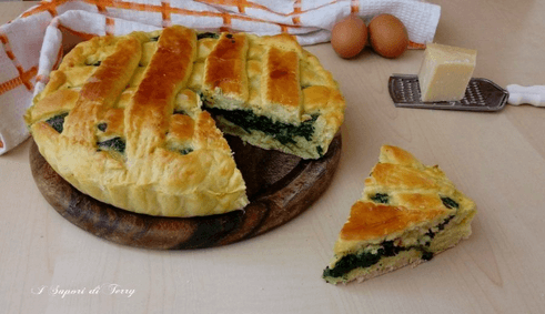 Homemade Italian savory pie filled with spinach and cheese, served on a wooden board with a slice cut out, with eggs, Parmesan, and a kitchen towel in the background.