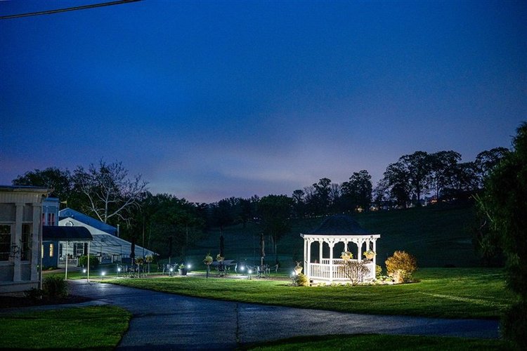 Outdoor wedding ceremony at a gazebo with guests seated and sunlight shining through the trees.
