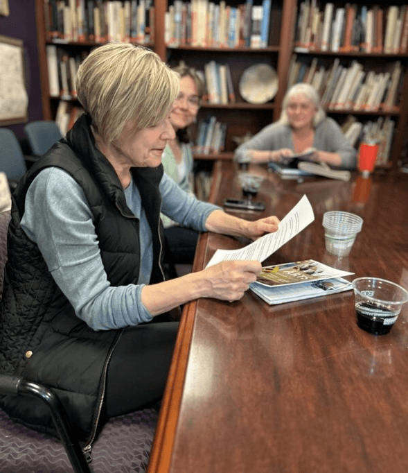 Woman reading a paper at a table during a writers’ open mic event.