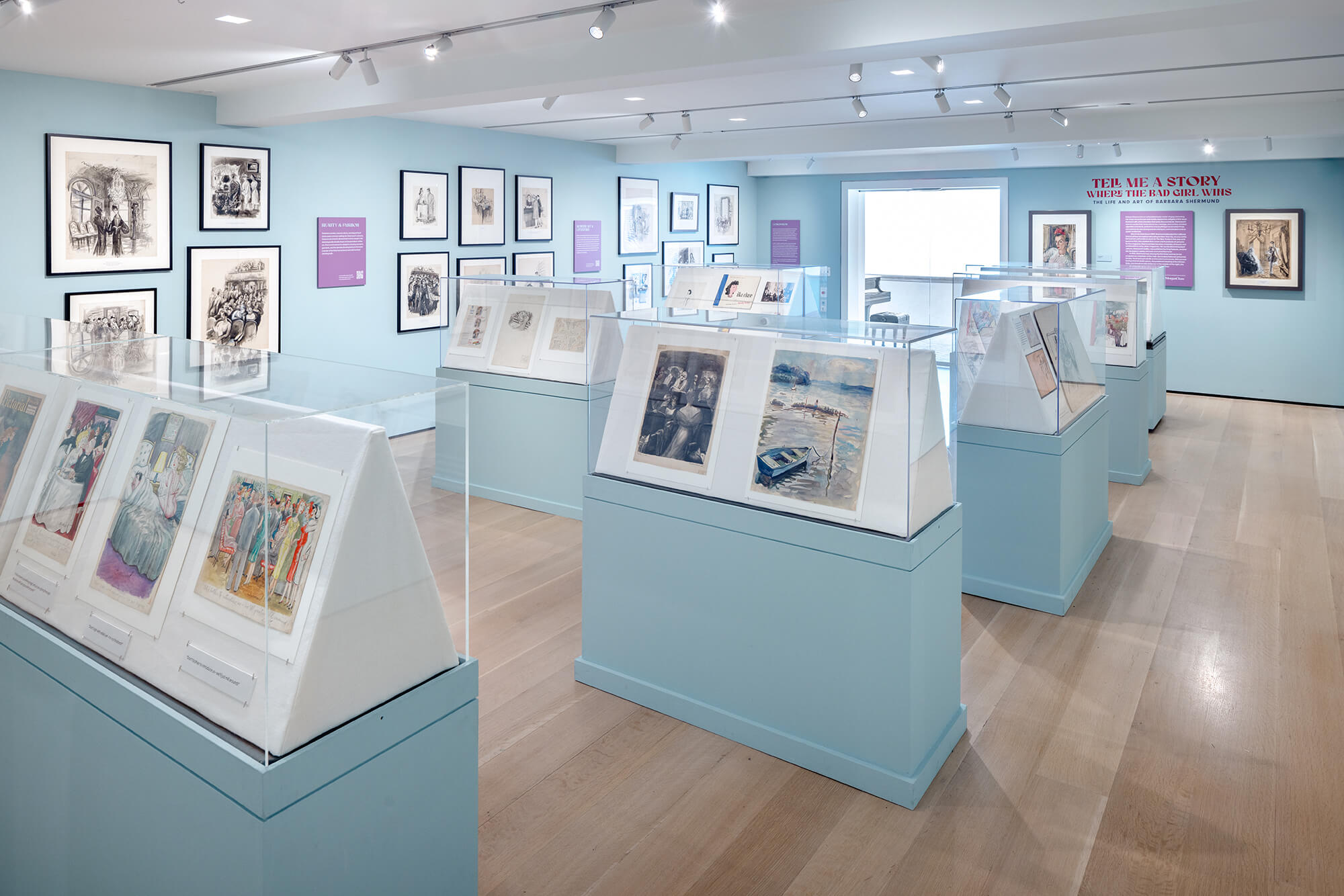 Art exhibition with framed works and illustrations displayed in glass cases.