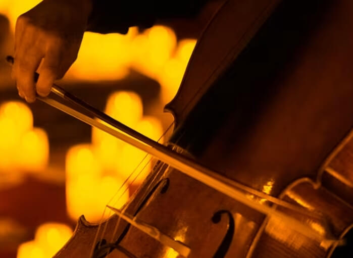 Close-up of a musician playing a cello with warm candlelight in the background.