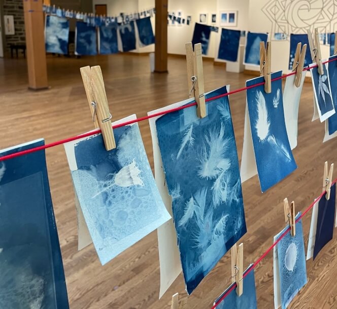 Blue cyanotype prints hanging on clotheslines in a gallery.